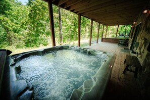 A hot tub with a wooden deck and a view of a forest.