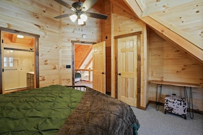 Ein Schlafzimmer einer Holzhütte mit einem Bett, einem Deckenventilator und einer Treppe, die zu einer oberen Ebene führt.