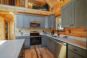 A modern kitchen with grey cabinets, stainless steel appliances, and a wooden floor.