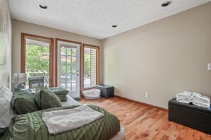 A bedroom with a bed, a bench, a suitcase, and a view of the outdoors.