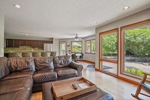 A spacious living area with a leather sofa, wooden coffee table, and large windows offering a view of the outdoors.