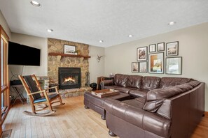 Ein Wohnzimmer mit Kamin aus Stein, einem Ledersofa, einem Holzschaukelstuhl und gerahmten Bildern an der Wand.