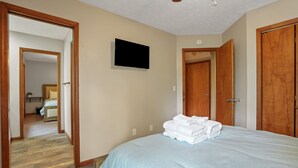 A bedroom with a bed, a television, wooden doors, and a hallway leading to another room. - Deer Ridge Lodge | Hocking Hills, Sleeps 26, Pool (Laurelville)