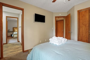 A bedroom with a bed, a television, wooden doors, and a hallway leading to another room.