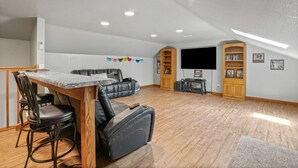 A spacious living area with a dining table, black leather sofa, and a flat-screen TV mounted on the wall. - Deer Ridge Lodge | Hocking Hills, Sleeps 26, Pool (Laurelville)