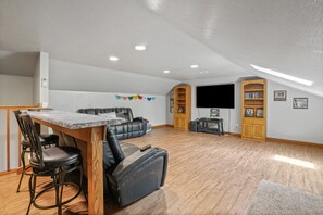 A spacious living area with a dining table, black leather sofa, and a flat-screen TV mounted on the wall. - Deer Ridge Lodge | Hocking Hills, Sleeps 26, Pool (Laurelville)