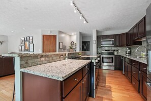 A modern kitchen with granite countertops, stainless steel appliances, and dark wooden cabinets. - Deer Ridge Lodge | Hocking Hills, Sleeps 26, Pool (Laurelville)