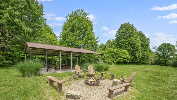 An outdoor seating area with a covered pavilion, wooden chairs, and a fire pit. - Deer Ridge Lodge | Hocking Hills, Sleeps 26, Pool (Laurelville)