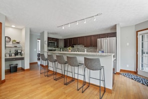 A modern kitchen with a central island, bar stools, and a microwave.