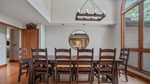 A dining area with a wooden table and chairs, a round mirror on the wall, and a chandelier. - Deer Ridge Lodge | Hocking Hills, Sleeps 26, Pool (Laurelville)