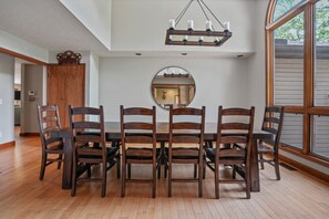 A dining area with a wooden table and chairs, a round mirror on the wall, and a chandelier.