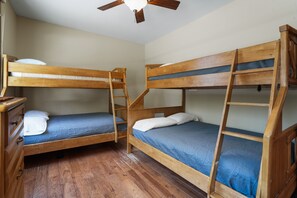 Une chambre avec deux lits superposés, un plancher en bois, un ventilateur de plafond et une commode.