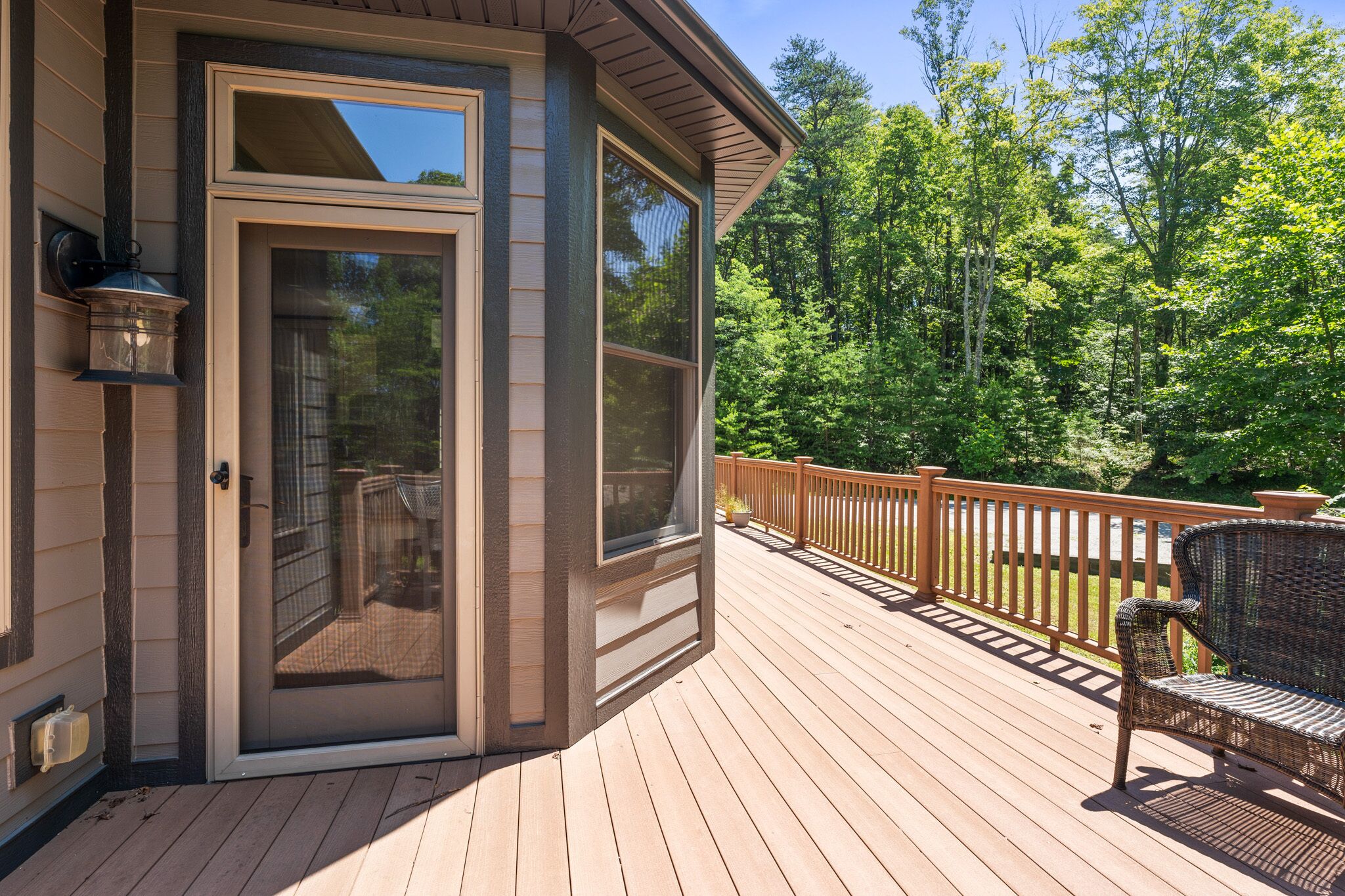 A wooden deck with a glass door leading to a covered outdoor area, surrounded by a wooden railing and trees.