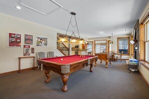 Une table de billard dans une pièce avec un escalier, des tableaux encadrés au mur et un porte-billes.