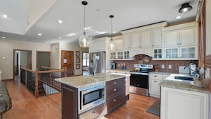 Una cocina amplia con encimeras de granito, electrodomésticos de acero inoxidable y muebles de color blanco.