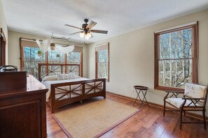 Un dormitorio con una cama de madera, un escritorio, una silla y ventanas grandes que ofrecen vistas a árboles.