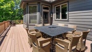 Un patio techado con una mesa y sillas, una terraza de madera y una casa con ventanas y puerta amplias.