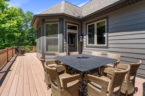 Un patio techado con una mesa y sillas, una terraza de madera y una casa con ventanas y puerta amplias.