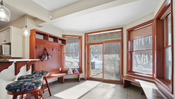 Una cocina con taburetes de madera, un banco y ventanas amplias que dan a un paisaje nevado.
