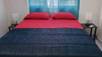 A bed with a red and blue bedspread, two bedside tables with lamps, and a window with blue curtains.