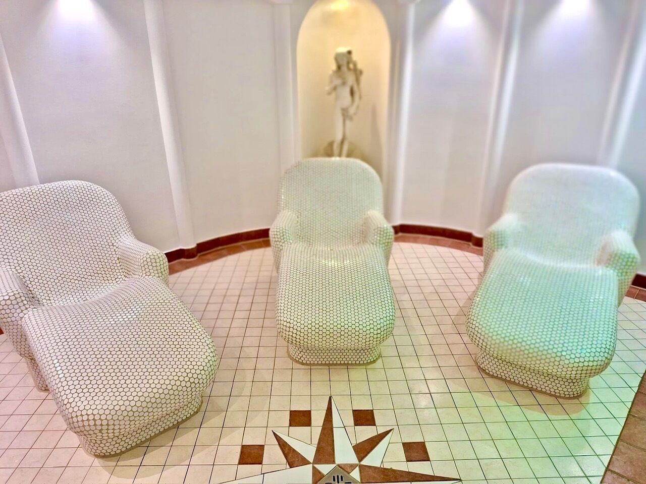 A room with three chairs covered in a textured fabric, a geometric floor pattern, and a central decorative element.