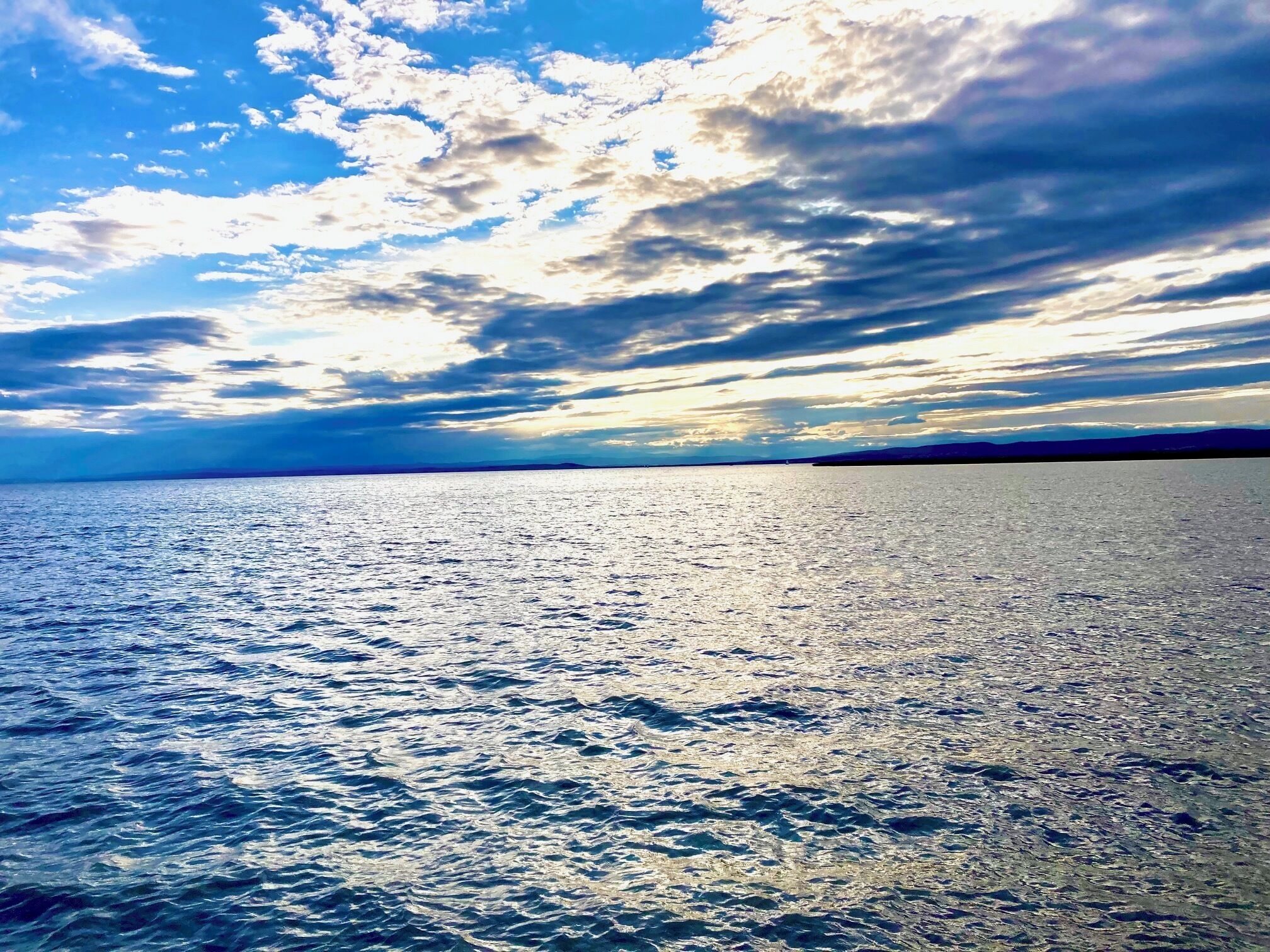 Mar calmo com céu claro e nuvens esparsas.