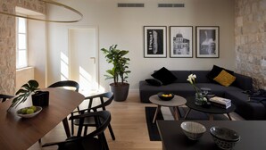 A modern living room with a dining area, featuring a stone wall, a sofa with cushions, a coffee table, and a potted plant.