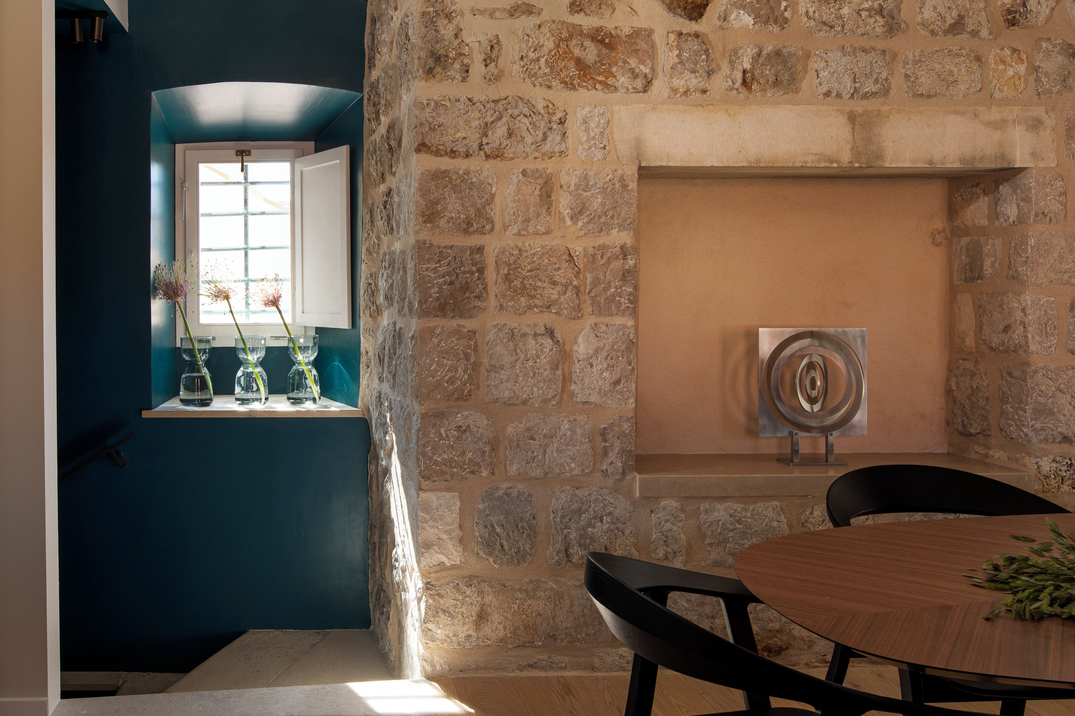 A room with a stone wall, a fireplace, a round wooden table, and a window with a view.