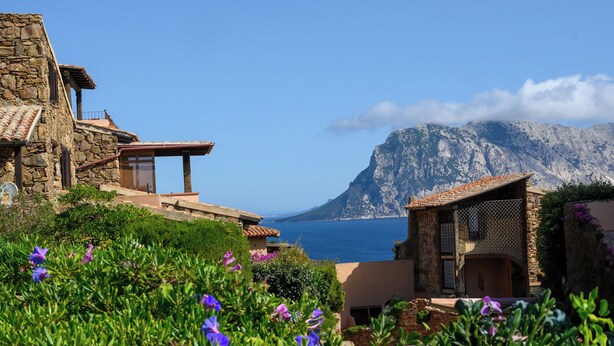 A coastal property with stone buildings, a view of the sea, and a mountain in the background. - Blue Dawn - Holiday home with cozy terrace, garden & wonderful sea view. (Capo Coda Cavallo)