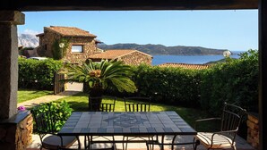 A patio with a table and chairs, a stone building in the background, and a view of the sea. - Blue Dawn - Holiday home with cozy terrace, garden & wonderful sea view. (Capo Coda Cavallo)