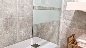 A bathroom with a glass shower enclosure, a wooden chair, and a toilet paper holder. - Madrid Suites Brand new apartment - 4 (Madrid)