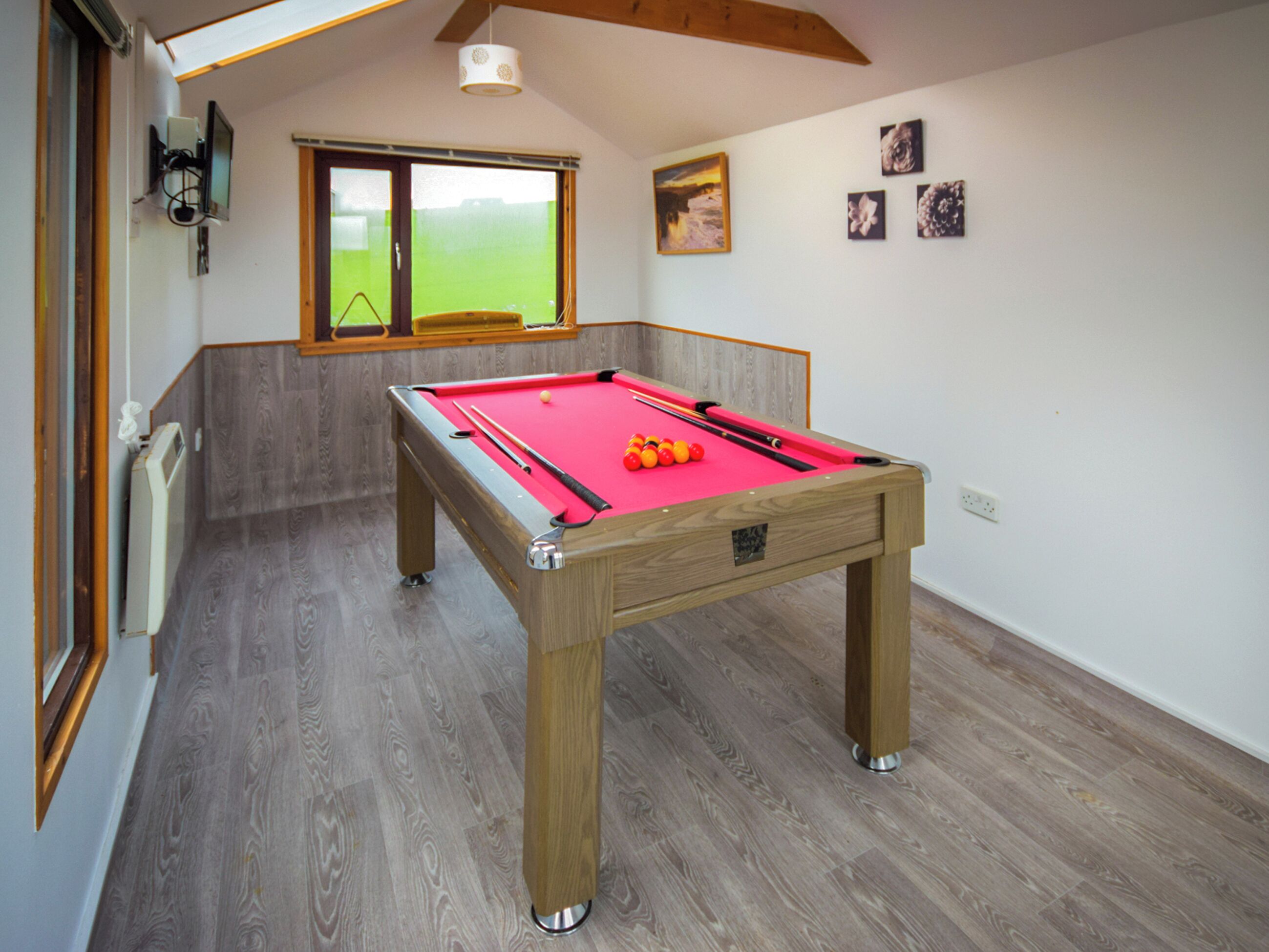 A pool table in a room with wooden flooring and a window with a view.