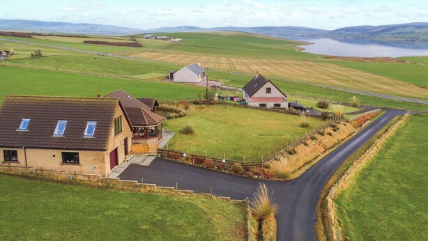 A rural landscape with a winding road, a small house with a red roof, and a body of water in the distance.