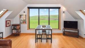 A modern loft bedroom with a large skylight, a dining area with a table and chairs, a bookshelf, and a television.