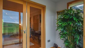 A wooden door leading to a dining area with a table and chairs, a potted plant, and a small dog figurine on a mat.