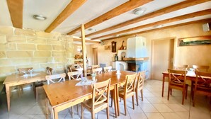 A rustic dining area with wooden tables and chairs, stone walls, and a stone fireplace.