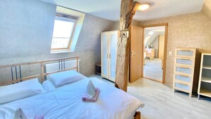 A bedroom with a large bed, a wooden wardrobe, a desk, and a skylight.