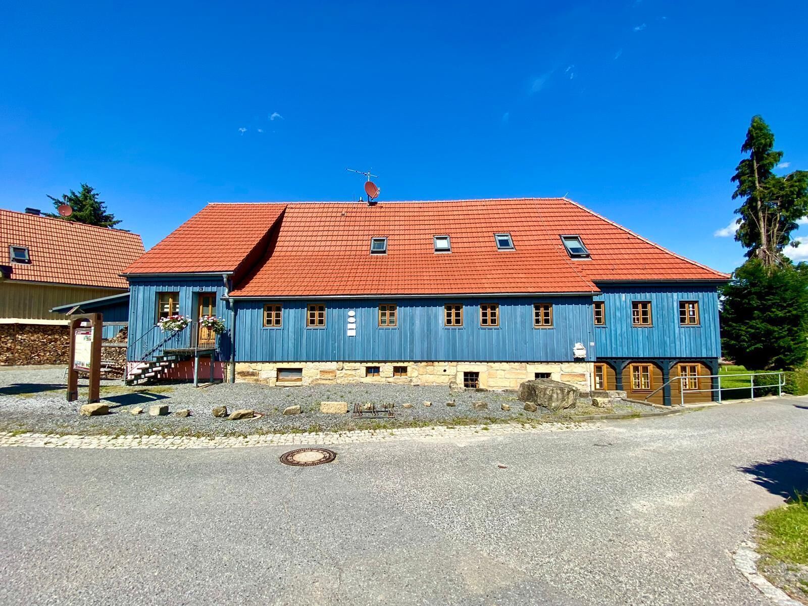 A traditional building with a red roof and blue walls, featuring a central entrance with steps and a small porch area.