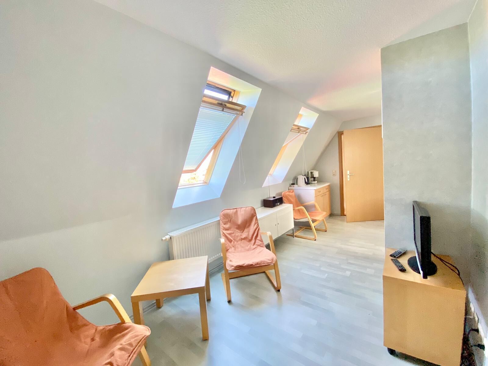 A modern, well-lit room with a sloped ceiling, two skylights, a desk, a chair, and a television on a cart.