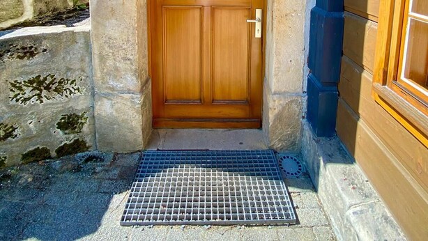 A wooden door with a metal grate in front, set in a stone structure with a blue roof.