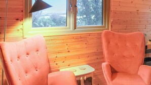 Ein Zimmer mit zwei rosafarbenen, gepolsterten Sessel, einem kleinen Holztisch und einem Fenster mit Blick auf Bäume.