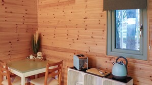 Ein Interieur einer Holzhütte mit einem Esstisch, Stühlen, einem Fenster, einem Toaster und einem Wasserkocher.
