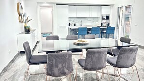 A modern dining area with a glass table and grey upholstered chairs, a kitchen in the background, and a view of the outdoors. - Luxury Penthouse Seaview Whit Terrace
 Giardini Naxos/Taormina (Giardini Naxos)