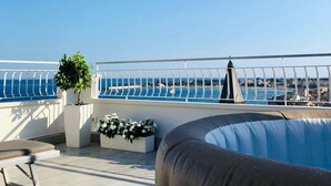 A rooftop terrace with a view of the sea, a white railing, a potted plant, and a cushioned seating area. - Luxury Penthouse Seaview Whit Terrace
 Giardini Naxos/Taormina (Giardini Naxos)