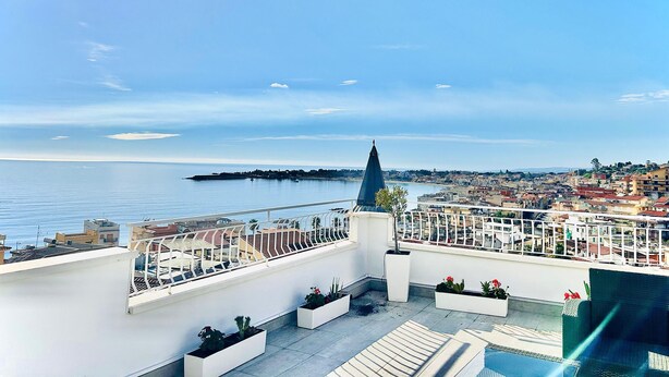 A rooftop terrace with a view of the sea and a distant cityscape. - Luxury Penthouse Seaview Whit Terrace
 Giardini Naxos/Taormina (Giardini Naxos)