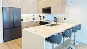 Une cuisine moderne dotée d’un grand îlot central, de tabourets de bar et d’appareils électroménagers intégrés.