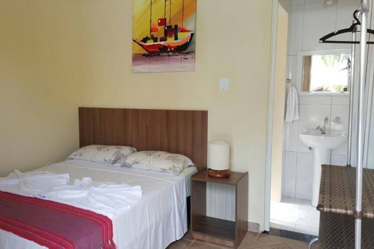 A bedroom with a bed, a nightstand, a hanging lamp, and a bathroom with a sink and mirror.