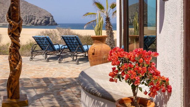 Een terras met uitzicht op de oceaan, een houten sculptuur, een bloempot en twee loungesteunen.