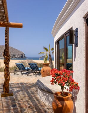 Een terras met uitzicht op de oceaan, een houten sculptuur, een bloempot en twee loungesteunen.