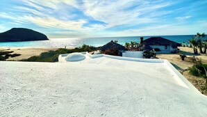 Een strand met rieten hutten, een zandvlakte en uitzicht op zee en een eiland in de verte.